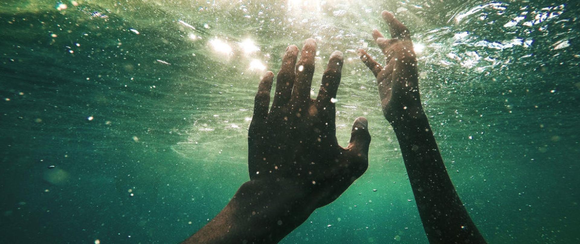 Zdjęcie dłoni w wodzie osobo tonącej.