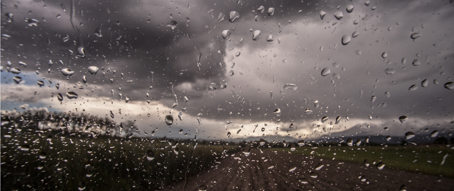 Okno pełne kropel wody, w tle deszczowy ciemny krajobraz
