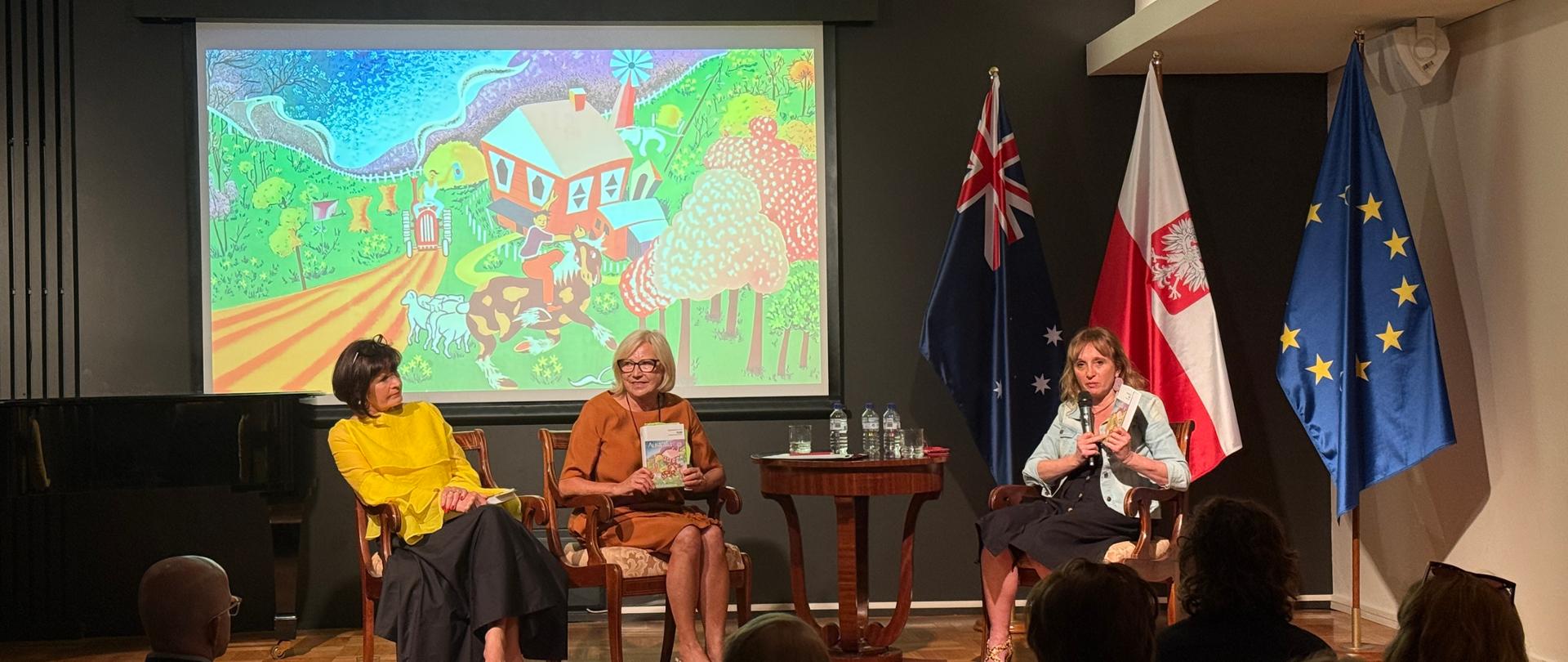 There are three women on stage; two of them are holding a book
in their hands. The audience is facing the stage.
