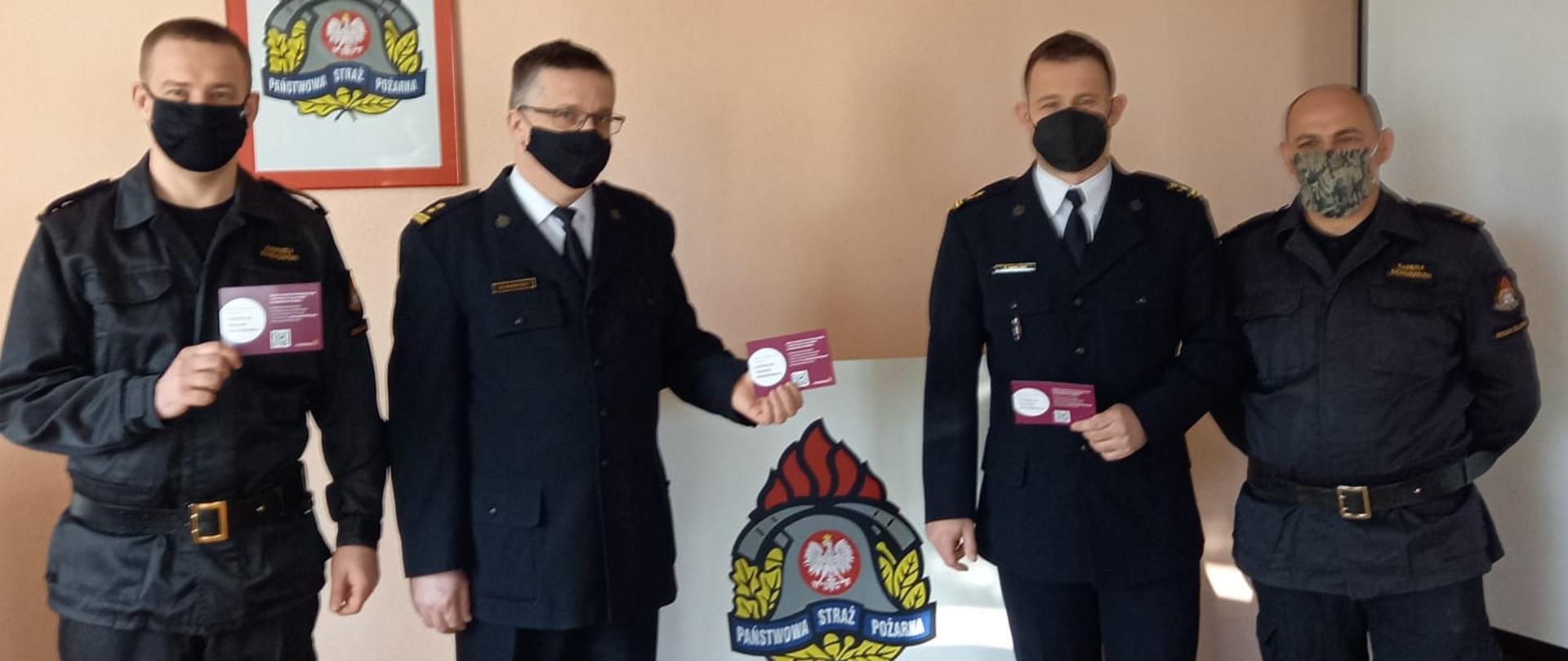 strażacy z Komendy Powiatowej w Środzie Śląskiej po szczenieniu z dokumentem potwierdzającym przyjęcie pierwszej dawki 