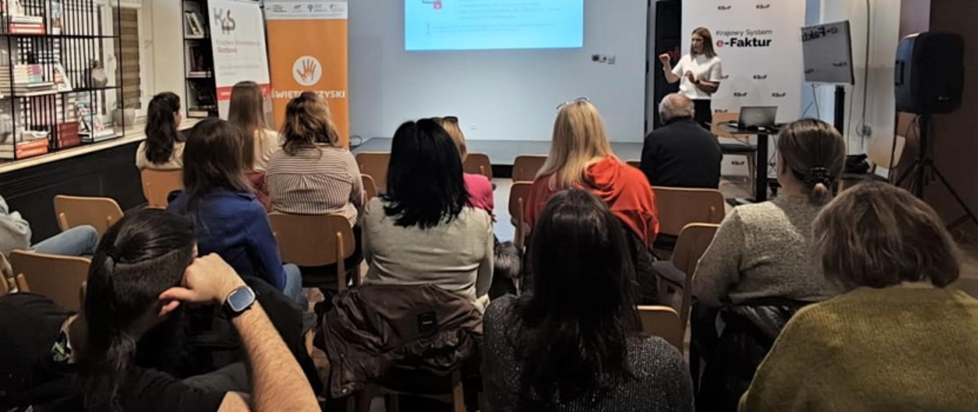 W sali grupa osób słucha wykładu o podatkach