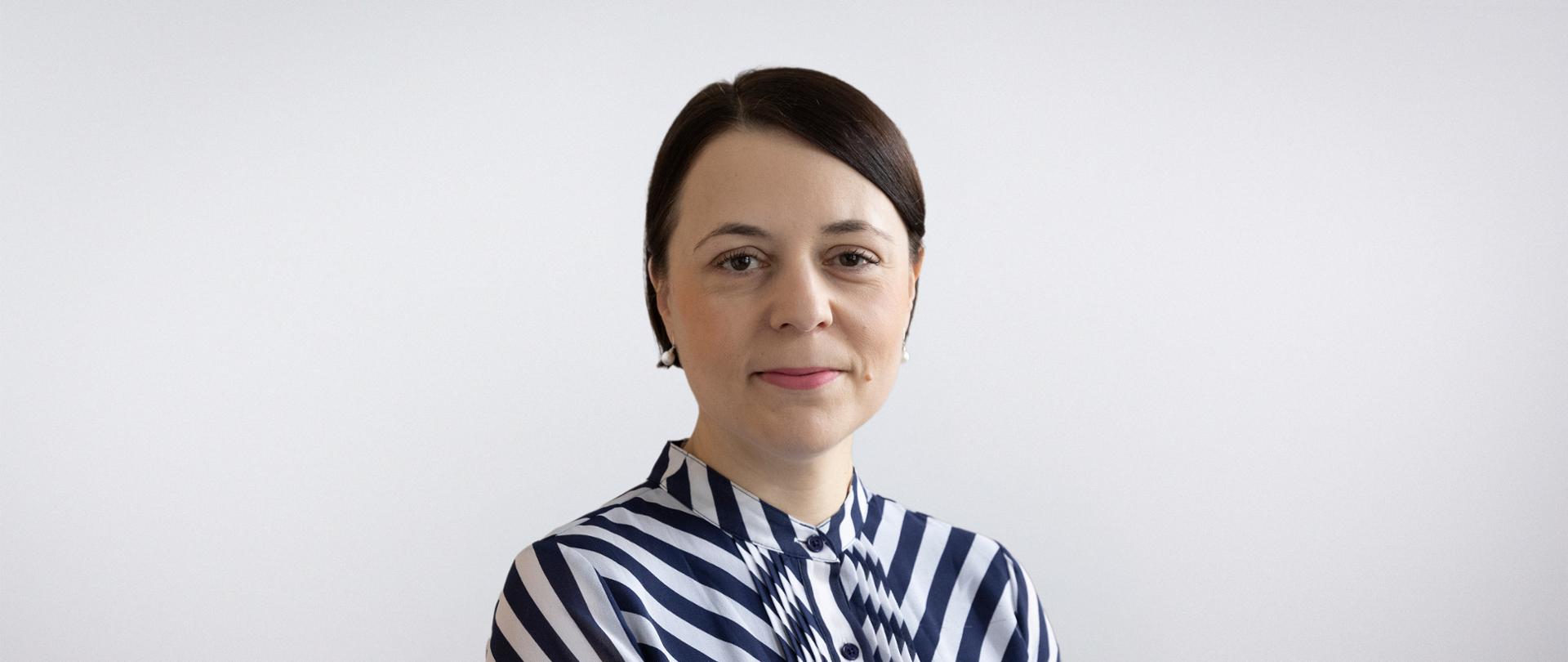 Portret Anny Błaszczak-Banasiak - uśmiechnięta kobieta z krótkimi, czarnymi włosami w bluzce w biało-granatowe pasy 