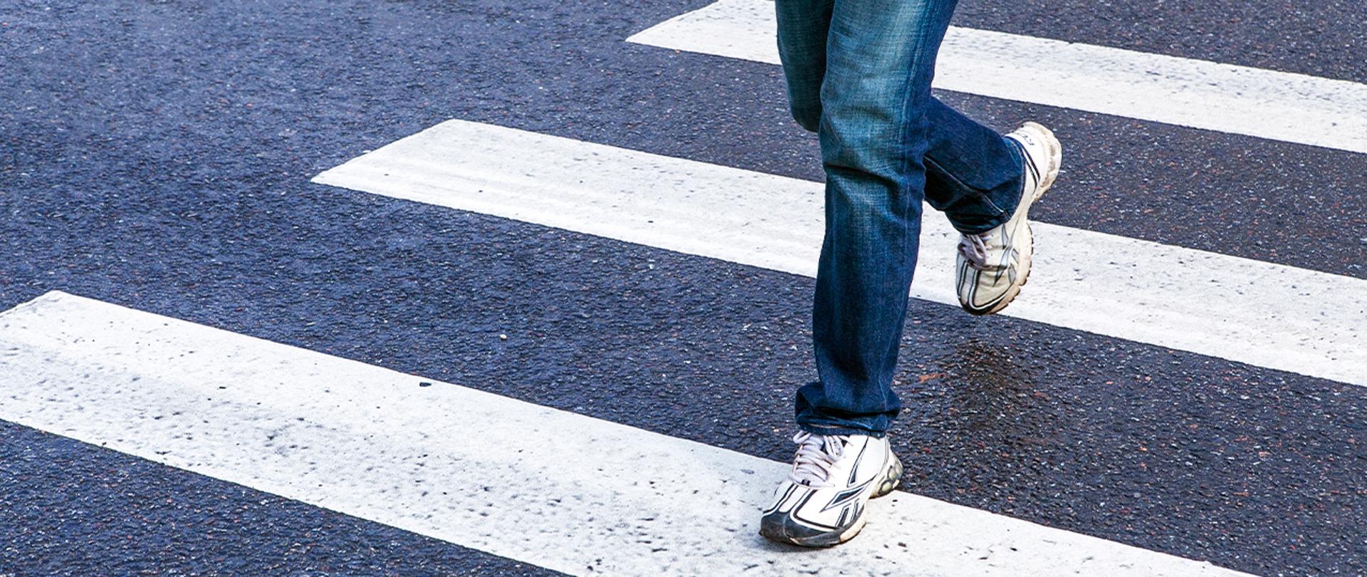 Na zdjeciu widoczne są nogi osoby przechodzącej przez przejście dla pieszych.
