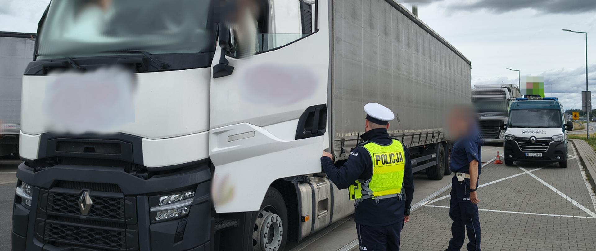 Ciężarówka z białą kabiną i naczepą. Obok stoją umundurowanie policjanci.