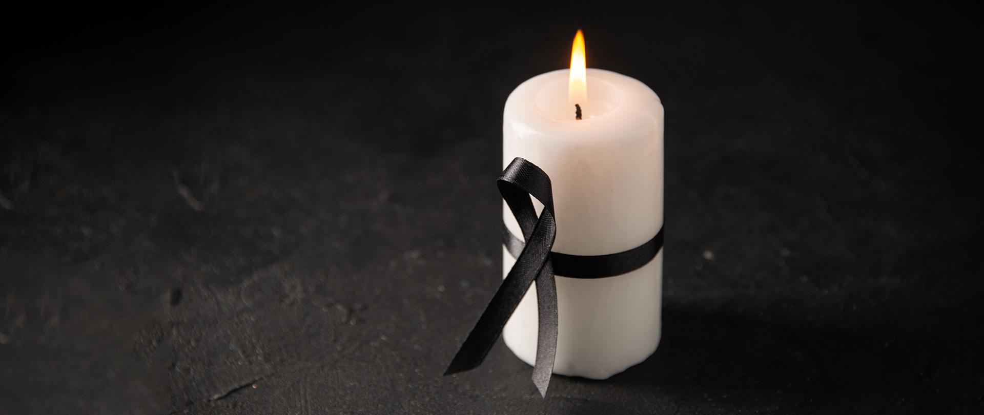 Świeca obwiązana żałobną wstążką.