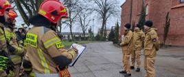 Zdjęcie przedstawia strażaków PSP oraz OSP ubranych w ubrania specjalne koloru piaskowego oraz w hełmy koloru czerwonego oraz białego, podczas ćwiczeń obiektowych w kościele Parafii Rzymskokatolickiej Wniebowzięcia NMP