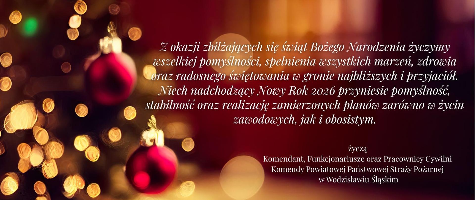 Świąteczna kartka z ciepłym, rozmytym tłem w odcieniach czerwieni i złota. Po lewej stronie widoczna choinka z lampkami, złotą śnieżynką i czerwonymi bombkami. Po prawej stronie znajduje się herb Państwowej Straży Pożarnej oraz tekst życzeń bożonarodzeniowych i noworocznych od Komendanta, funkcjonariuszy i pracowników cywilnych Komendy Powiatowej PSP w Wodzisławiu Śląskim, z życzeniami pomyślności i realizacji planów w 2026 roku.