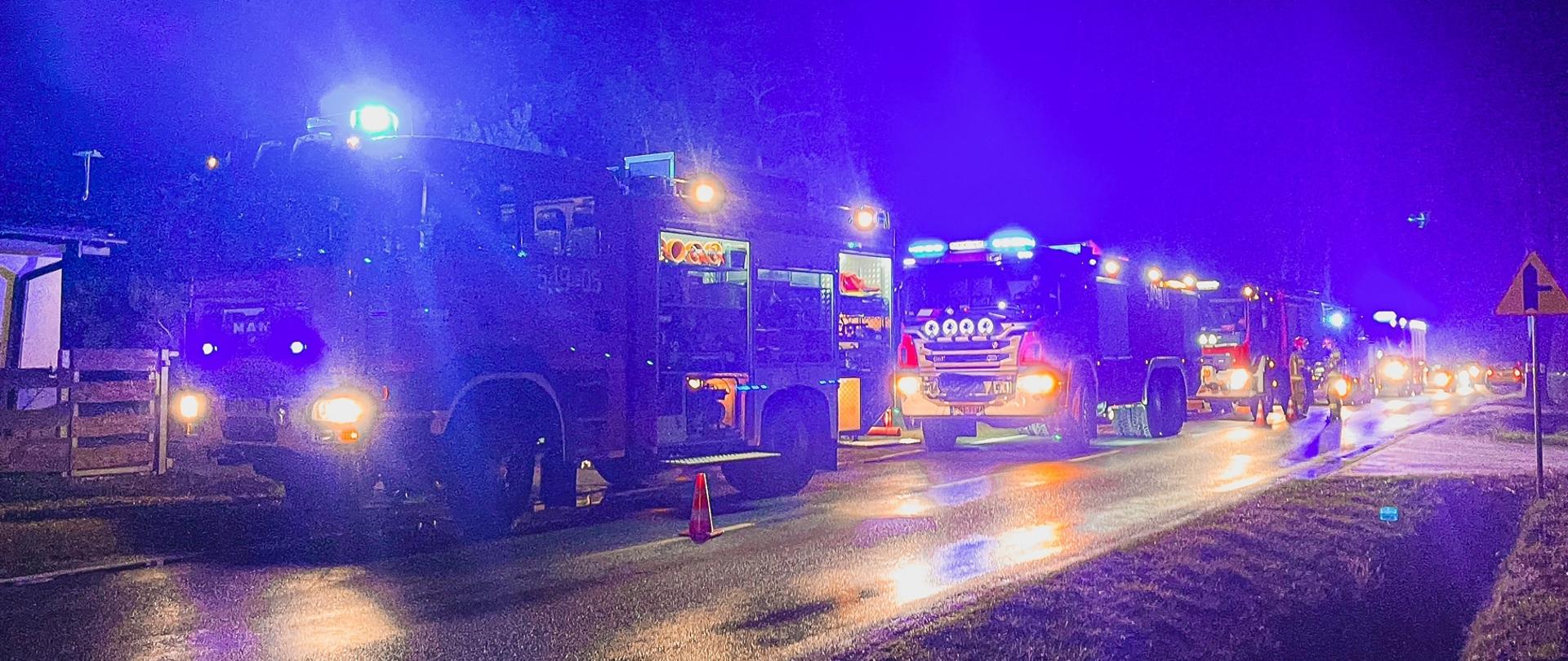 Na zdjęciu samochody strażackie stojące na jezdni w pobliżu palącego się budynku.