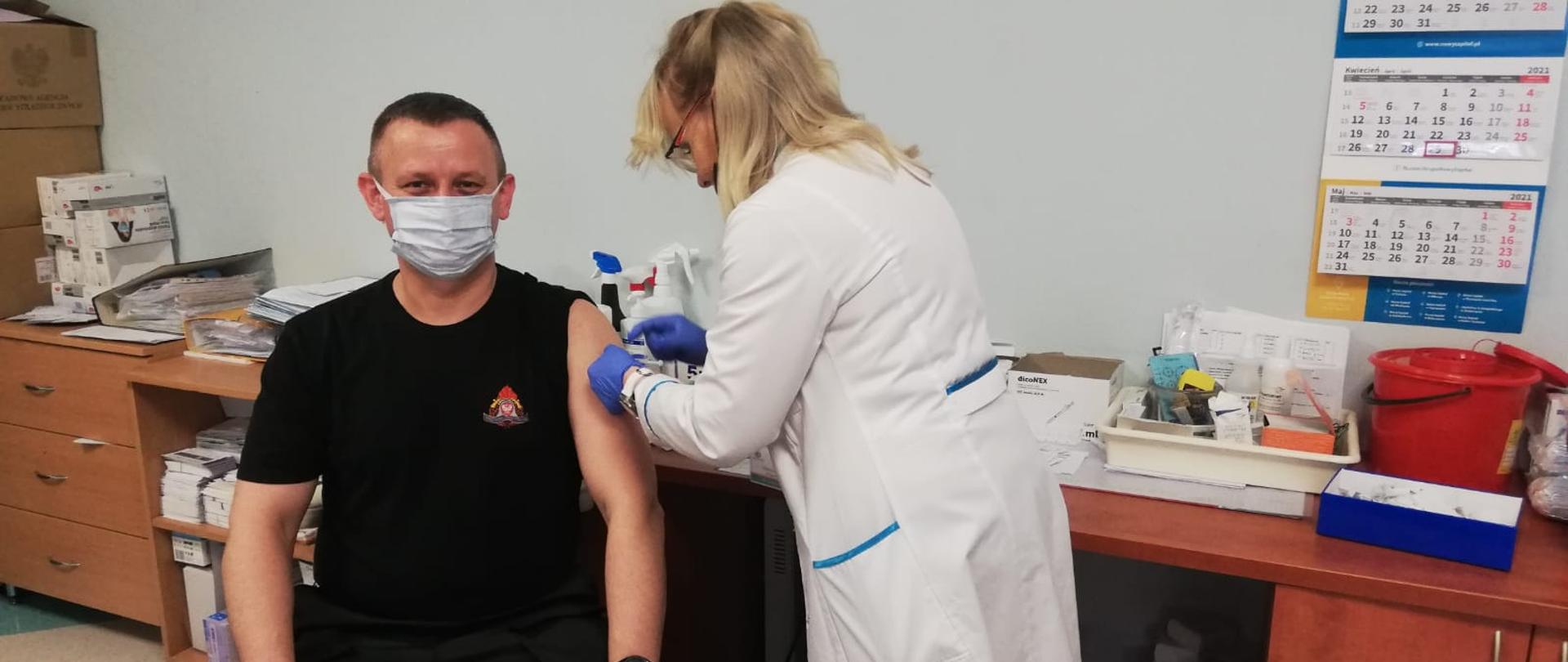 Na zdjęciu po lewej stronie młodszy brygadier Paweł Puchowski podczas szczepienia przeciw Covid-19. Po prawej pani pielęgniarka wykonująca szczepienie.