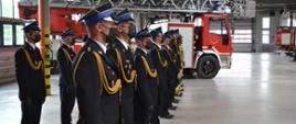 umundurowani strażacy w dwuszeregu na tle z pojazdem strażackim