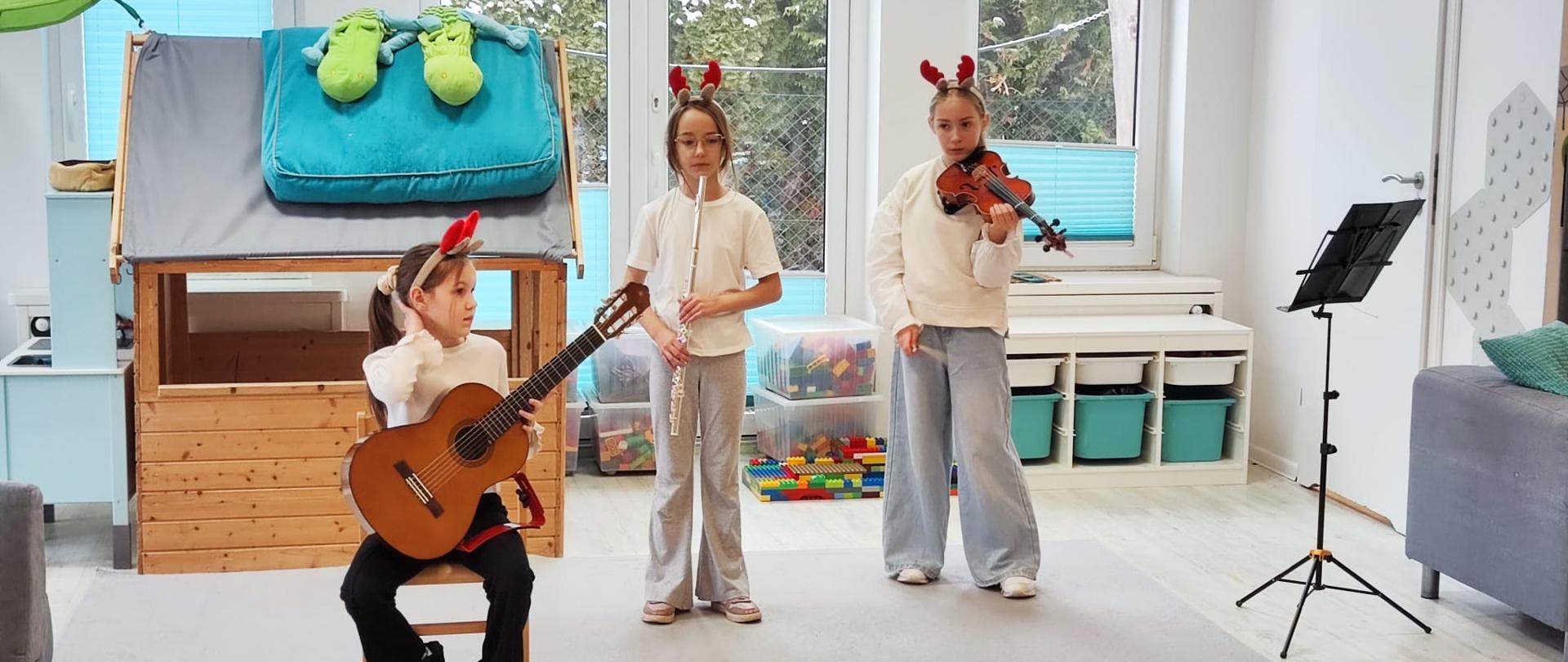 Uczennice ZPSM w przedszkolu grają na instrumetach (skrzypce, flet, gitara) w tle okna i domek dla dzieci