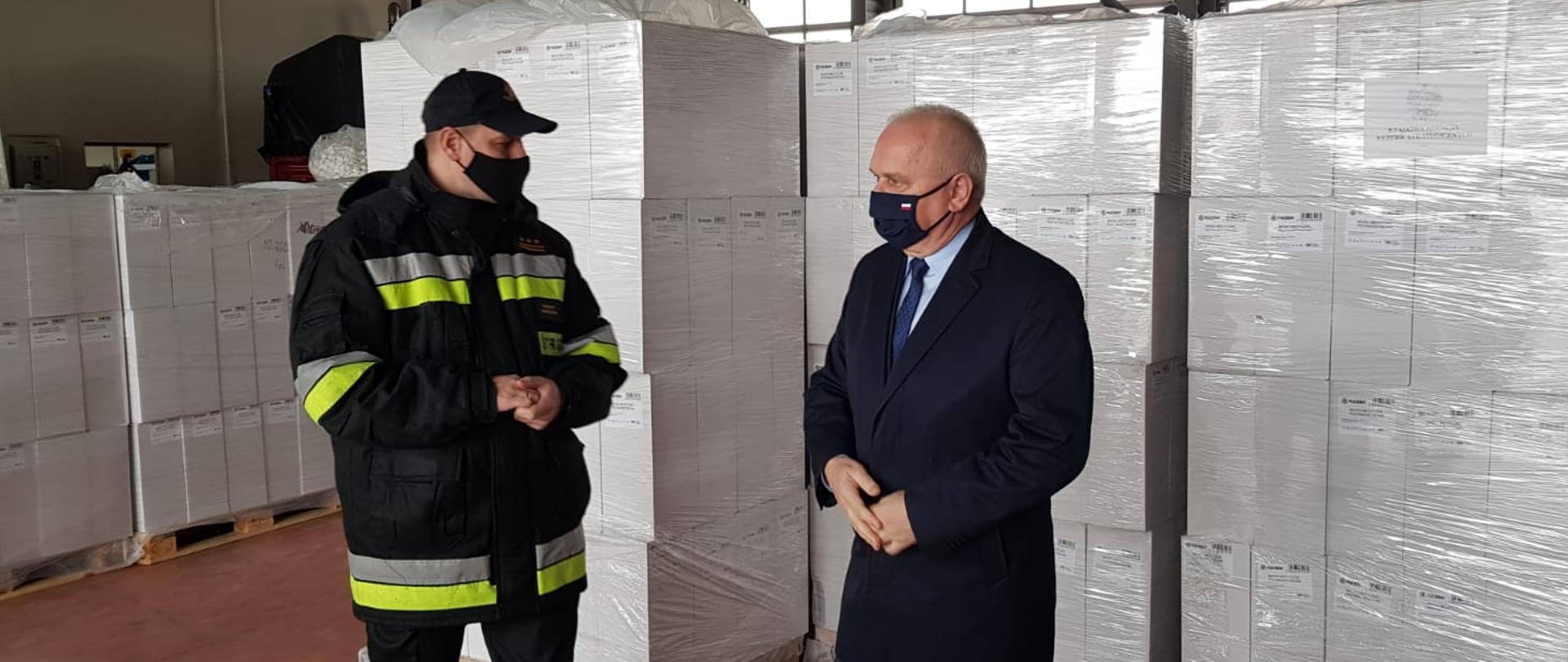 Zdjęcie przedstawia Lubuskiego Komendanta Wojewódzkiego PSP oraz Wojewodę Lubuskiego stojących na tle palet z maseczkami.