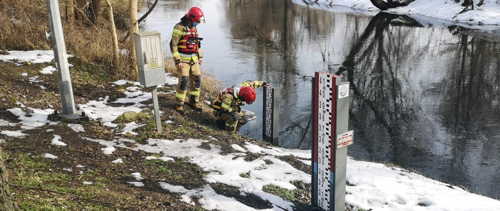 Dwóch strażaków nad brzegiem Drwęcy sprawdzają odczyt z wodowskazu.