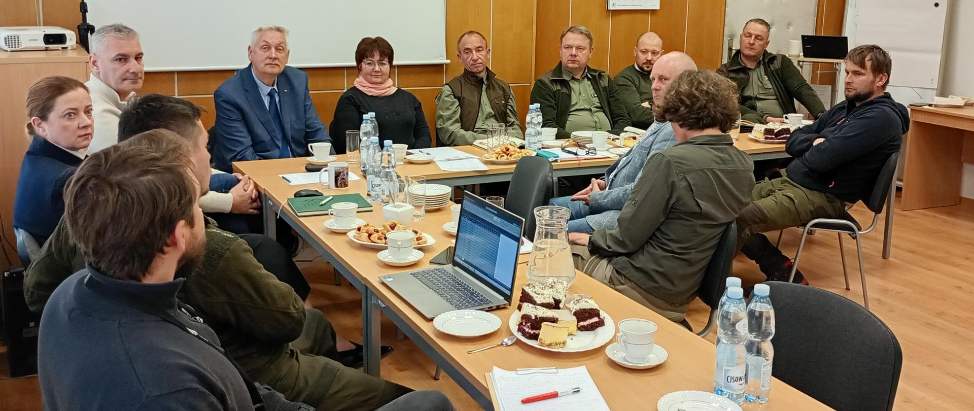 Na zdjęciu siedzą przy stole ustawionym w kształcie litery L przedstawiciele RDOŚ w Gorzowie Wielkopolskim, Uniwersytetu Zielonogórskiego, Urzędu Marszałkowskiego, Lasów Państwowych, Parku Narodowego „Ujście Warty” oraz Polskiego Związku Łowieckiego. Na stole notatniki, woda i ciasto oraz laptop. 