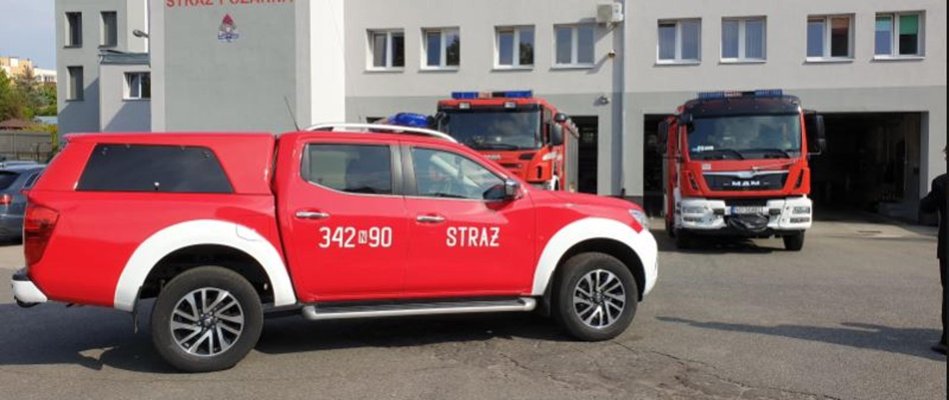 Zdjęcie przedstawia nowy pojazd marki Nissan Navara koloru czerwonego na tle budynku remizy Jednostki Ratowniczo Gaśniczej nr 2 w Elblągu. 