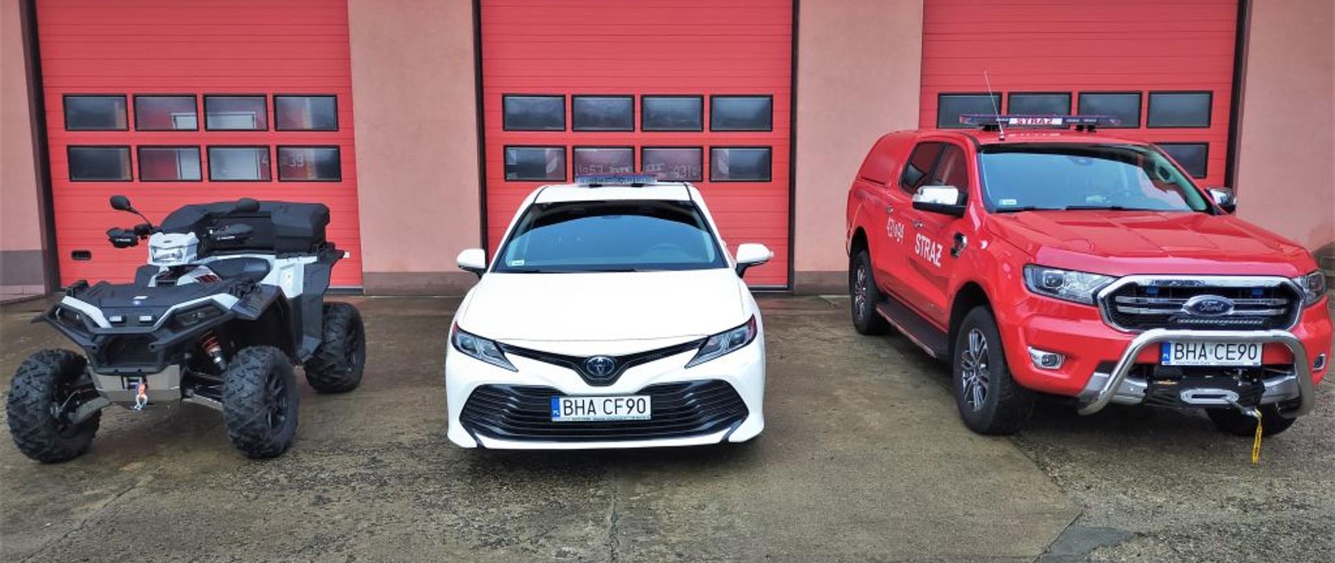 Na zdjęciu widoczne trzy pojazdy na tle bram garażowych JRG Hajnówka. od lewej quad, w środku toyota camry samochód operacyjny, z prawej samochód terenowy ford ranger. 