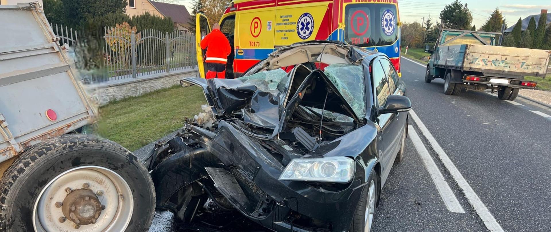 Uszkodzony pojazd osobowy. W tle karetka pogotowia.