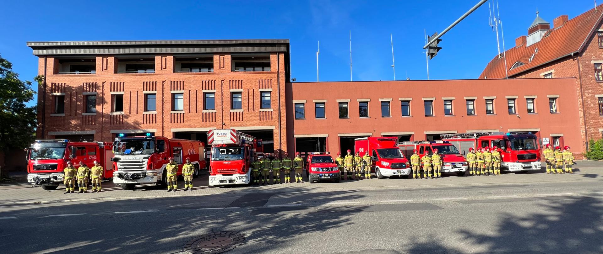 Zdjęcie zrobione przed strażnicą KP PSP w Gnieźnie. Na zdjęciu widać strażaków oraz samochody pożarnicze podczas oddawania hołdu tragicznie zmarłemu funkcjonariuszowi KG PSP