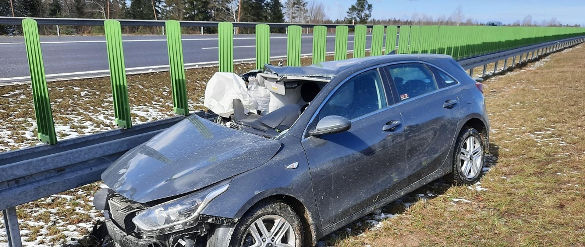 Na zdjęciu widać samochód osobowy marki Kia stojącego przy barierach ochronnych. Po uderzeniu w tył naczepy wystrzeliły w nim poduszki powietrzne oraz uszkodzony został przód pojazdu jak i jego prawy bok z licznymi. W samochodzie wypadła przednia szyba.