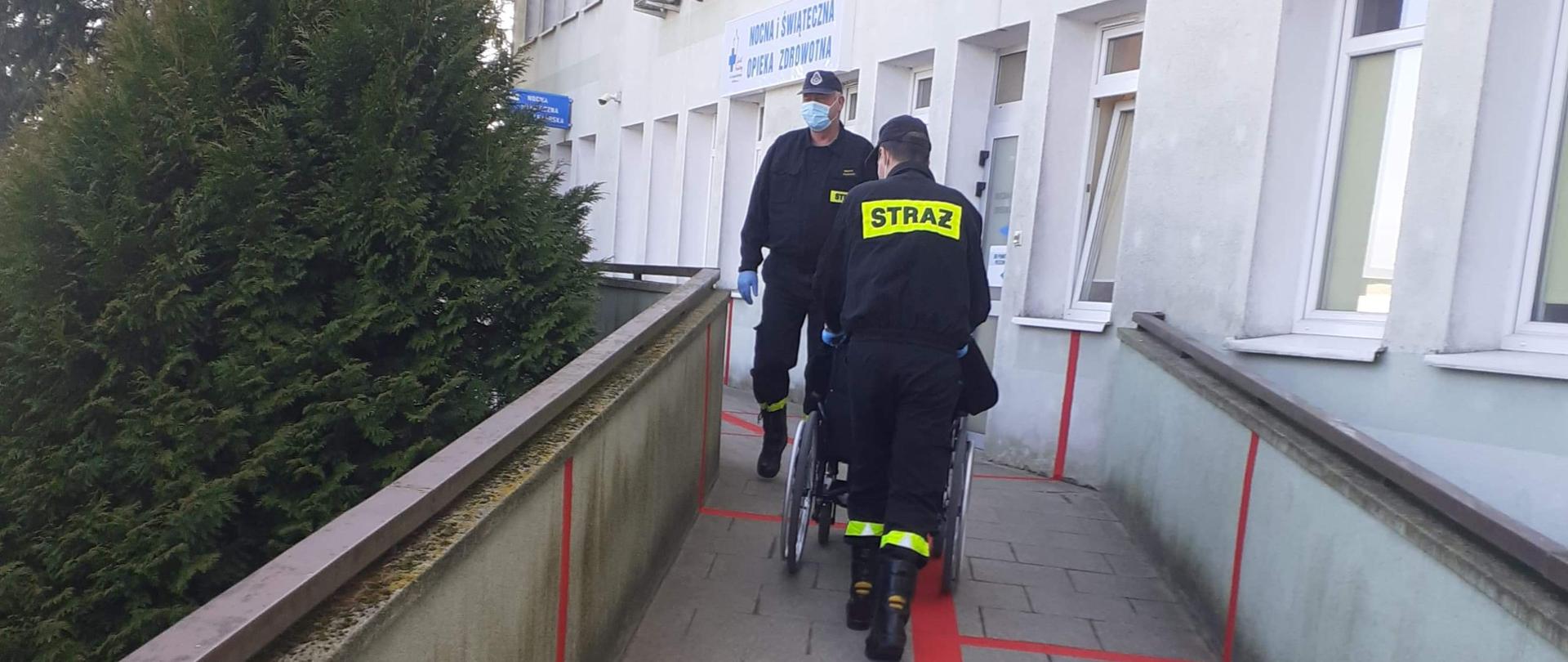 Na zdjęciu druhowie z seniorem jadącym do punktu szczepień na wózku inwalidzkim