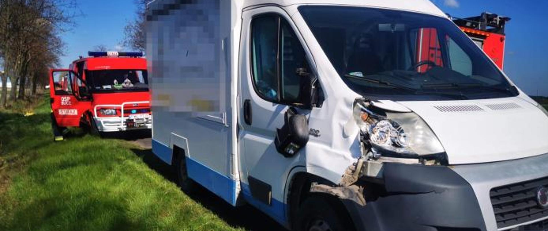 Pobocze drogi, rozbity samochód dostawczy, w tle wóz strażacki.