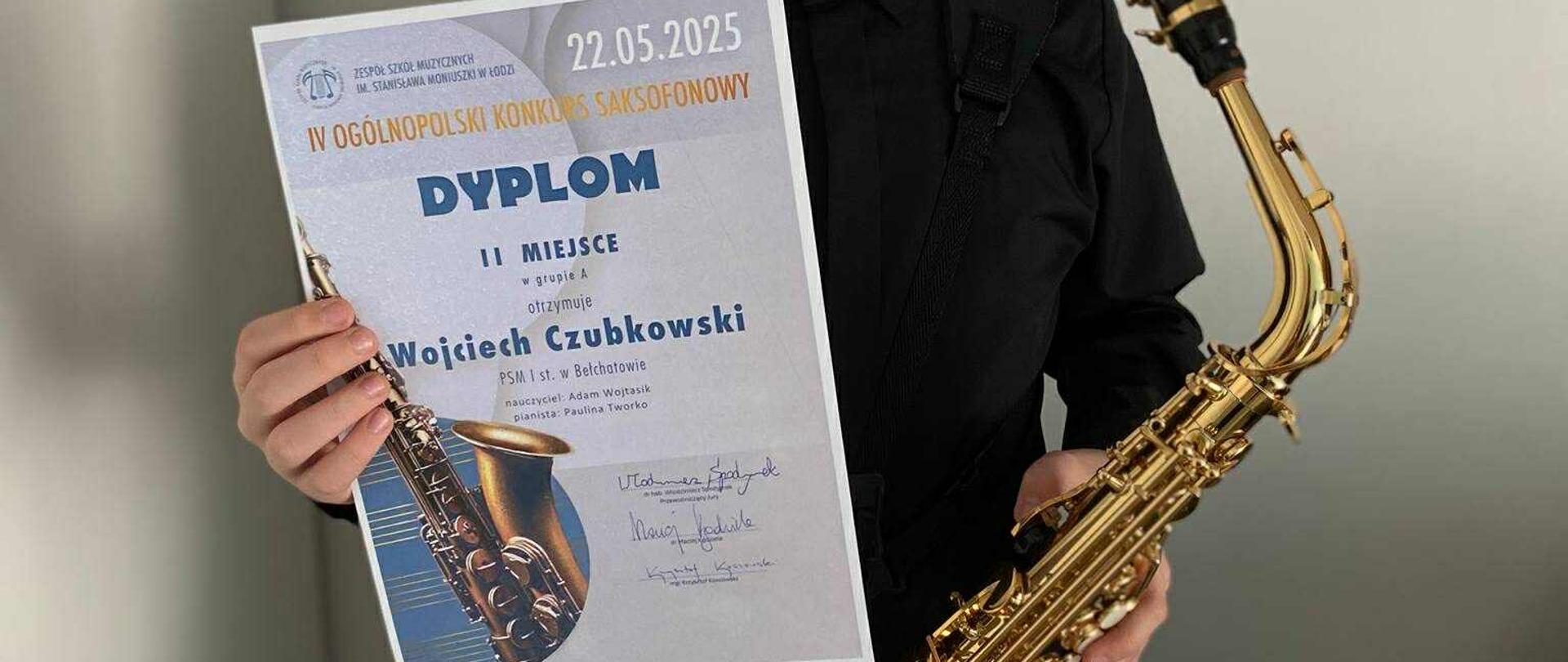 Na zdjęciu znajduje się chłopiec, który w prawej ręce trzyma dyplom, a w lewej saksofon.