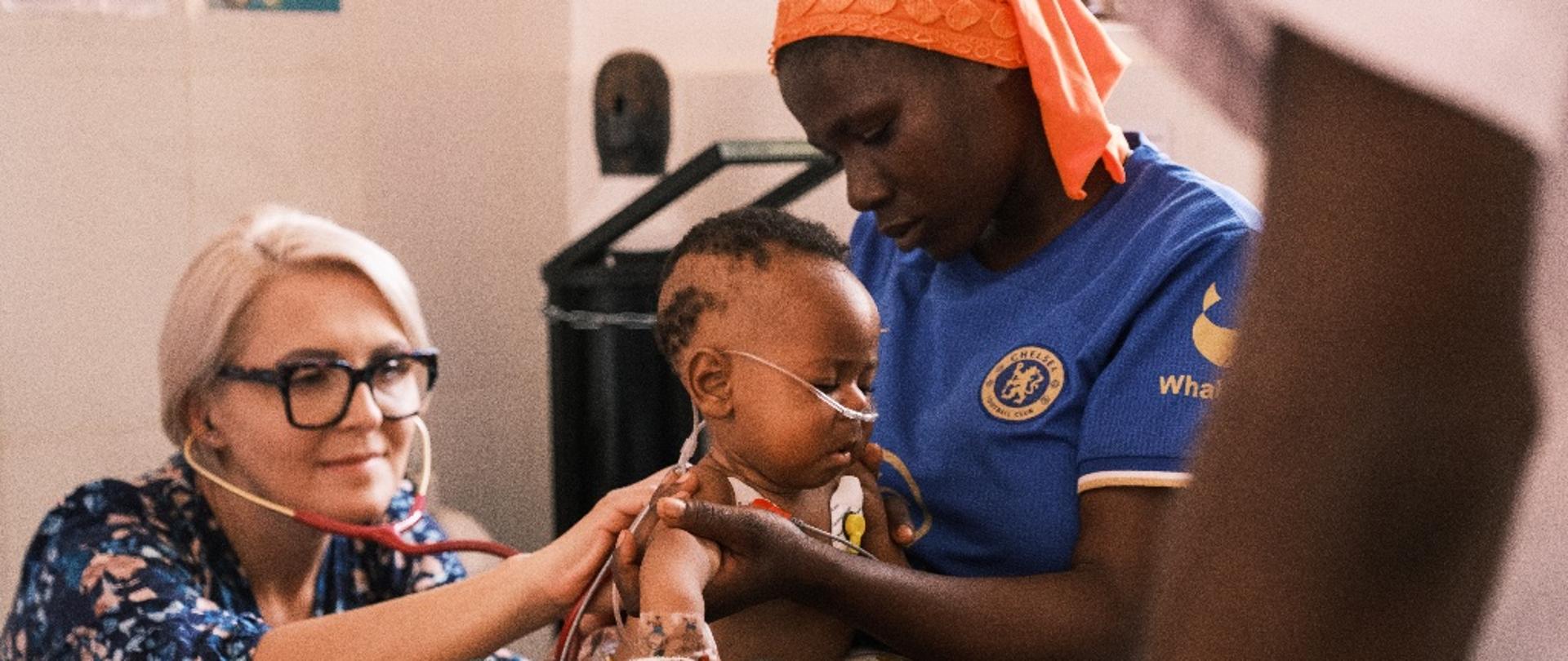 Lekarka osłuchuje małego chłopca, który siedzi na kolanach matki