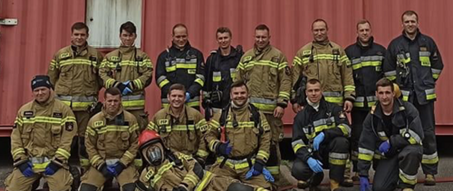 zdjęcie grupowe strażaków w ubraniach specjalnych za nimi kontener