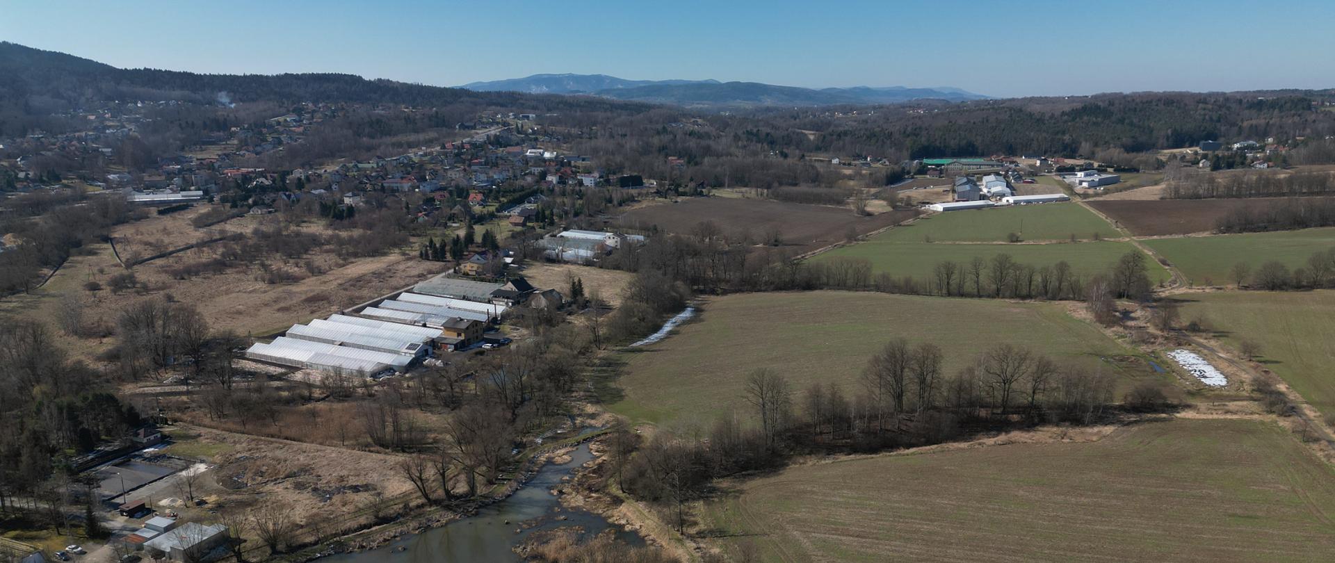 Węzeł Kalwaria Zebrzydowska, teren przyszłego węzła, na zdjęciu widoczny niewielki zbiornik wodny, zabudowania, zalesienia i pola, w oddali Beskidy