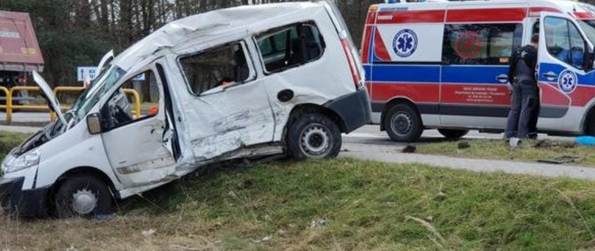 Zdjęcie przedstawia wrak samochodu osobowego na poboczu drogi oraz karetkę pogotowia