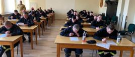 Zdjęcie przedstawia druhów w Sali szkoleniowej w trakcie egzaminu pod nadzorem strażaka PSP.
