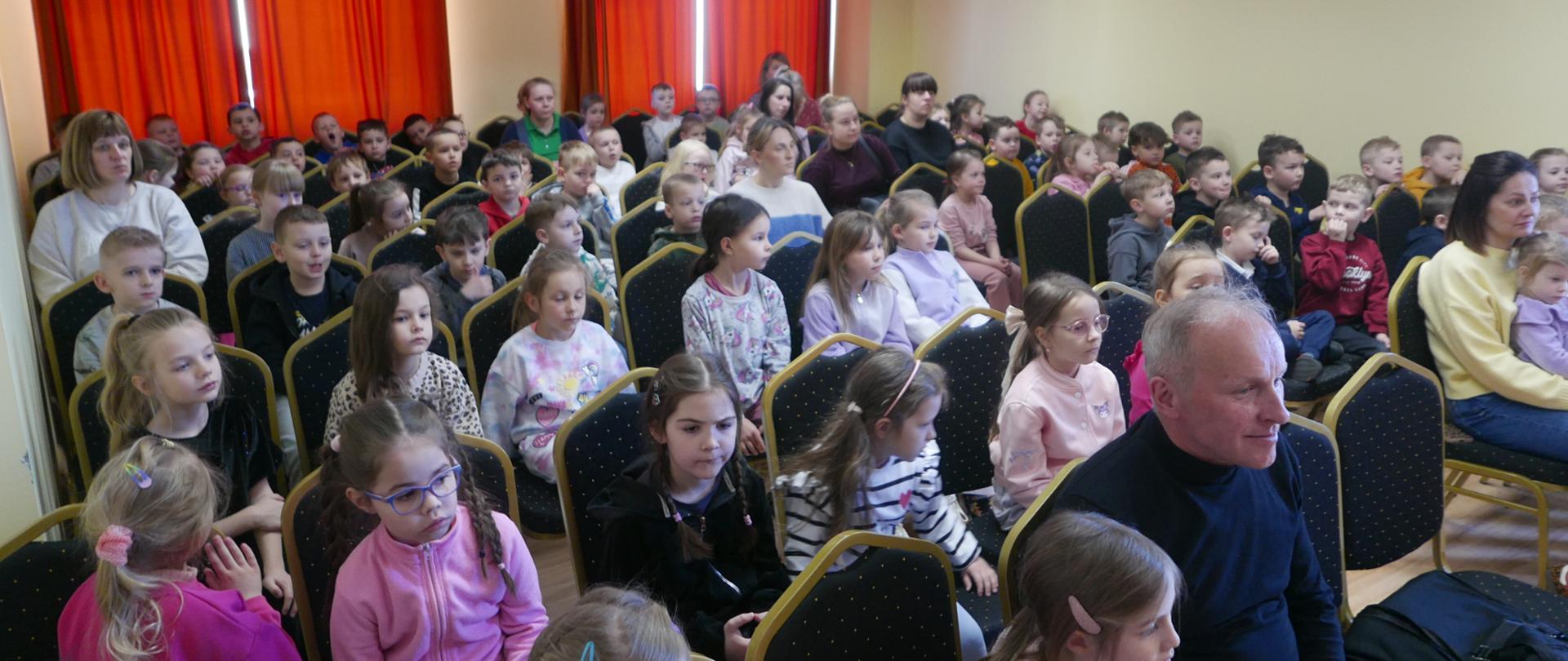 Dzieci z przedszkola siedzą w auli szkoły muzycznej podczas prezentacji starszych kolegów i koleżanek