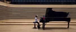 Dziewczynka gra na fortepianie na estradzie sali koncertowej.