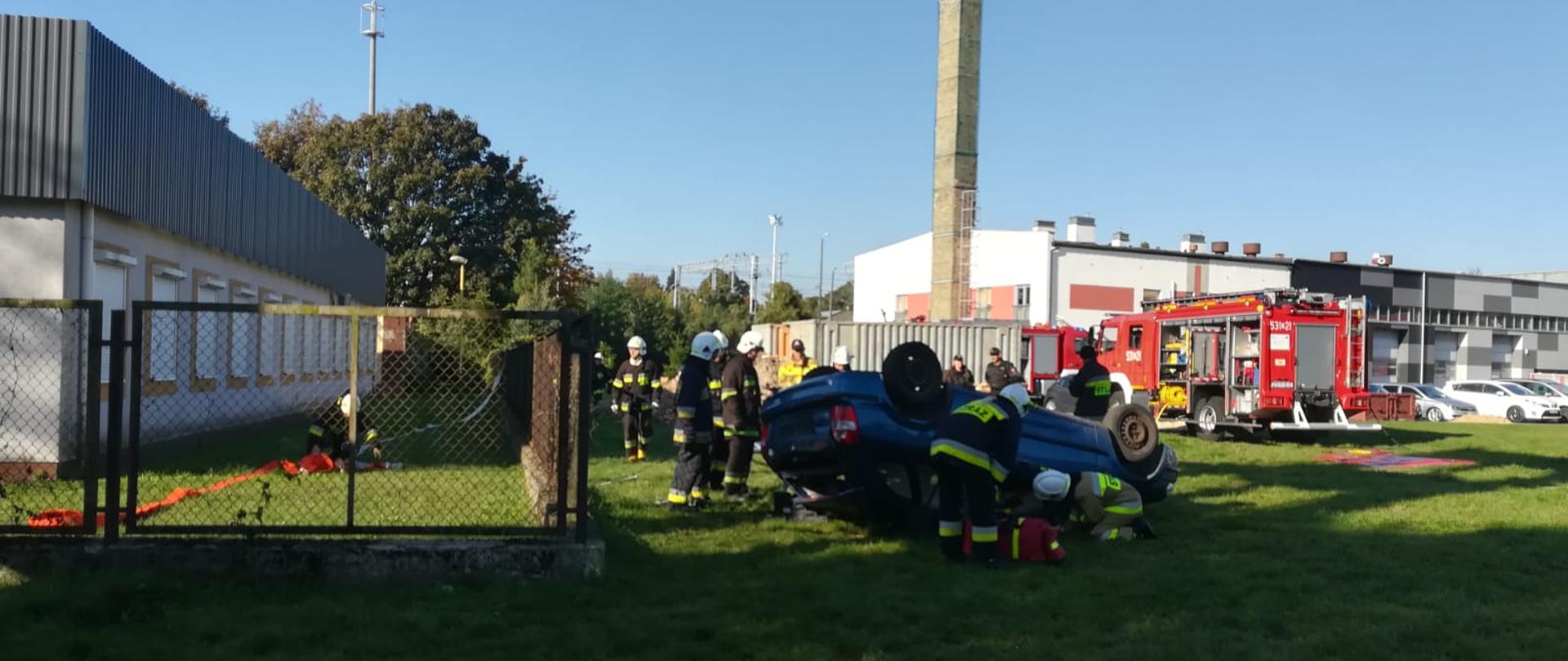 na pierwszym planie przewrócony samochód, dwóch egzaminowanych zajmuje się poszkodowanym.