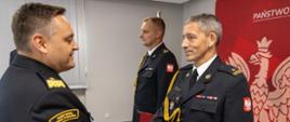Nadbryg. Krzysztof Kędryk wręcza akt powołania mł. bryg. Mariusza Strzelczaka na stanowisko Zastępcy Komendanta Powiatowego Państwowej Straży Pożarnej w Oleśnie. Strażacy w mundurach galowych. W tle widoczny mł. bryg. Szymon Jędrzejas oraz kawałek banneru Państwowej Straży Pożarnej."