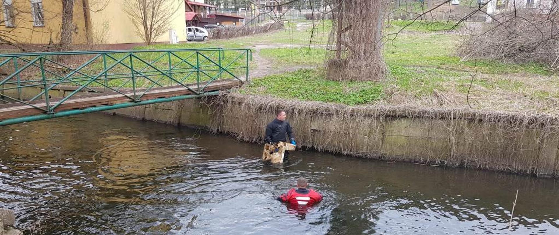 Strażacy ubrani w kombinezony nurkowe oczyszczają koryto rzeki Drwęcy ze śmieci.