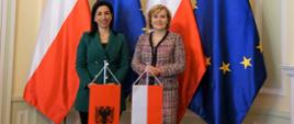 Wiceminister Anna Krupka oraz Evis Kushi, Minister Edukacji, Sportu i Młodzieży Republiki Albanii, stoją na tle flag Polski i Unii Europejskiej. Przed minister z Albanii ustawiony jest proporzec albański, a przed minister Krupką - polski.