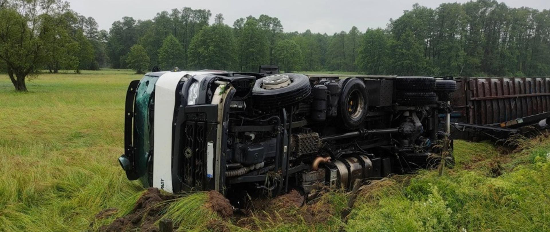 Na zdjęciu widać samochód ciężarowy marki Renault leżący poza jezdnią, na trawie, na prawym boku. 