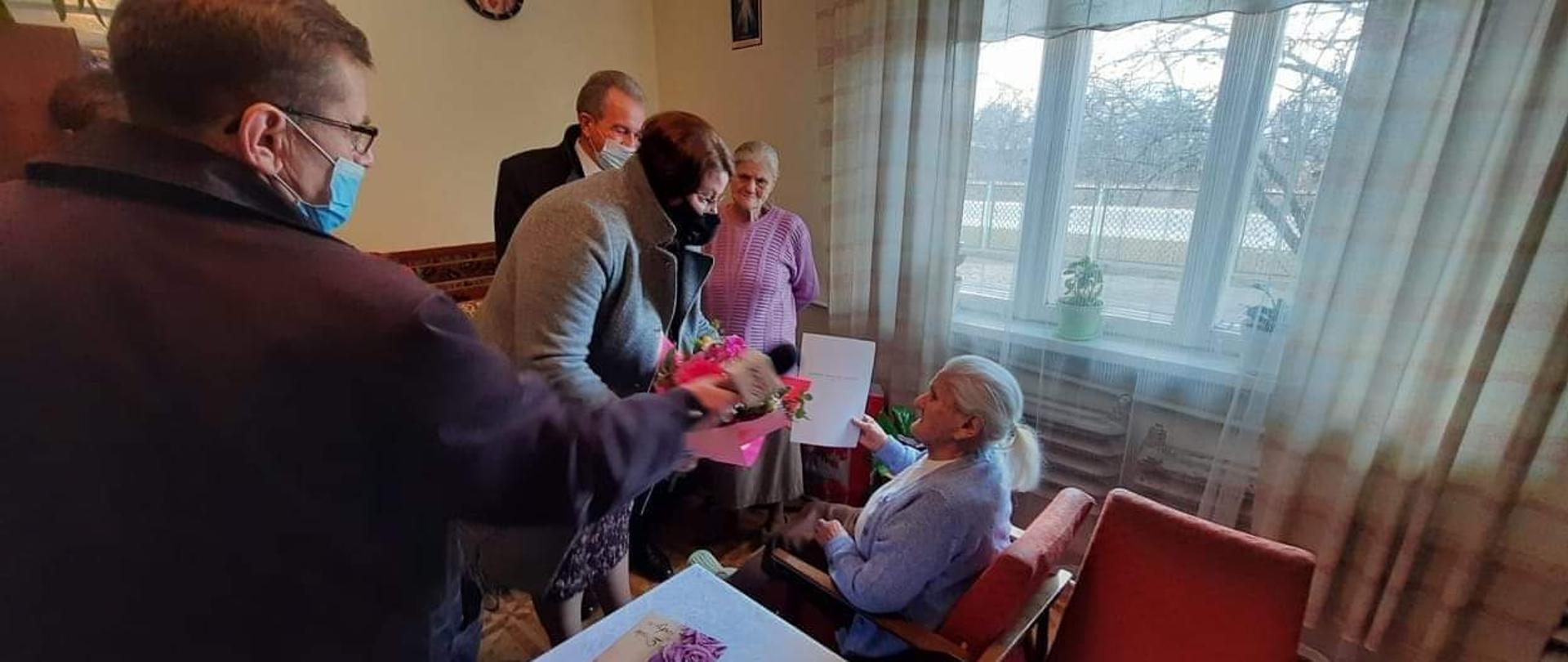 Na zdjęciu znajdują się cztery osoby, jedna wręcza kwiaty Jubilatce. 