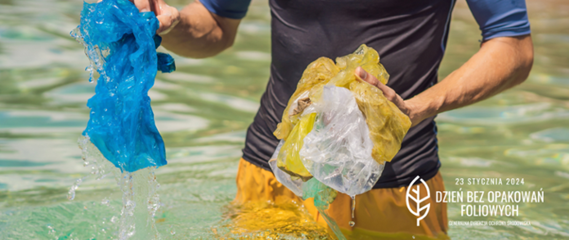 Mężczyzna w sportowym stroju stoi po biodra w wodzie,. W rękach trzyma ociekające wodą foliowe woreczki, które wyjął z wody.