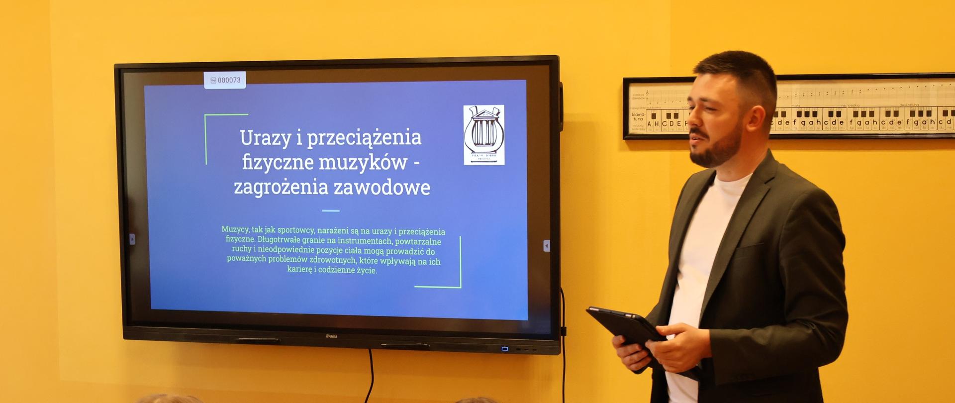 Mężczyzna stojący obok dużego ekranu multimedialnego.