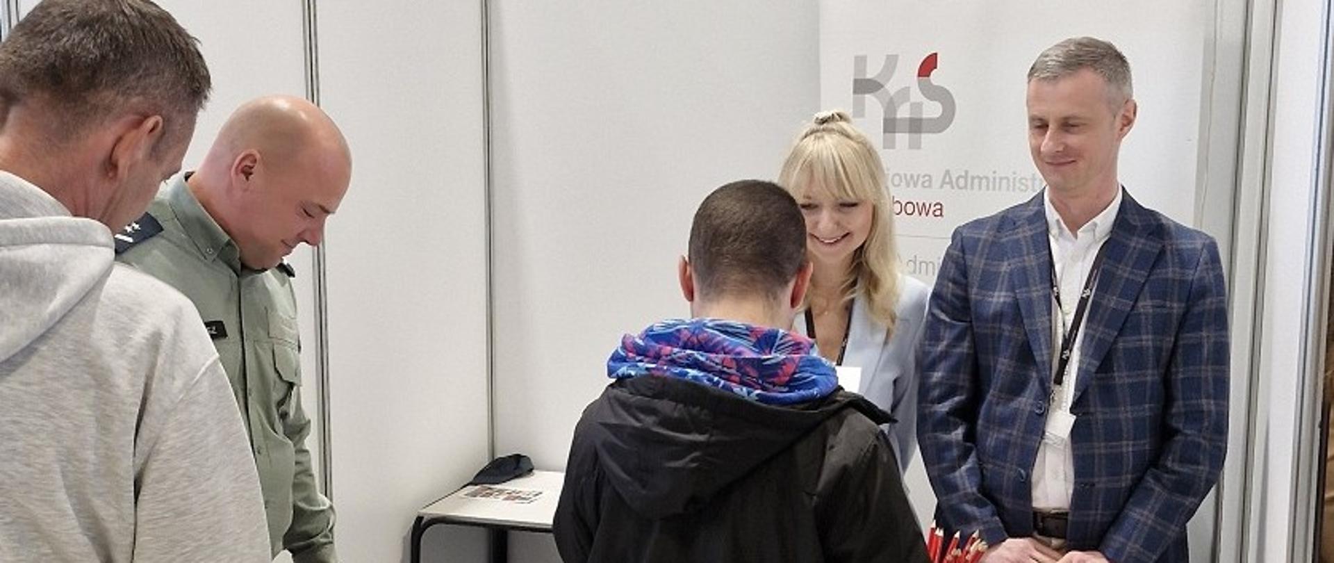 Przedstawiciele podkarpackiej KAS stoją przy stanowisku. Towarzyszy im pies służbowy. 