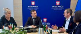 4 osoby rozmawiają przy stole konferencyjnym na tle ścianki wojewoda warmińsko-mazurski 