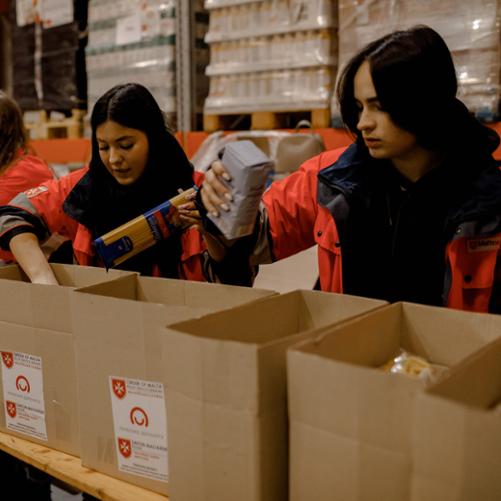 Na zdjęciu widać wolontariuszy znajdujących się w magazynie. Młodzież pakuje paczki żywnościowe dla potrzebujących. 