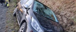 Zdjęcie przedstawia samochód osobowy, który wypadł z drogi i znajduje się w przydrożnym rowie. Samochód ma uszkodzoną przednią szybę. 