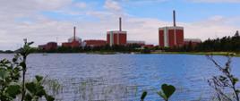 Elektrownia Jądrowa Olkiluoto - trzy budynki reaktorów stoją w pobliżu zbiornika wodnego oraz w otoczeniu zieleni.