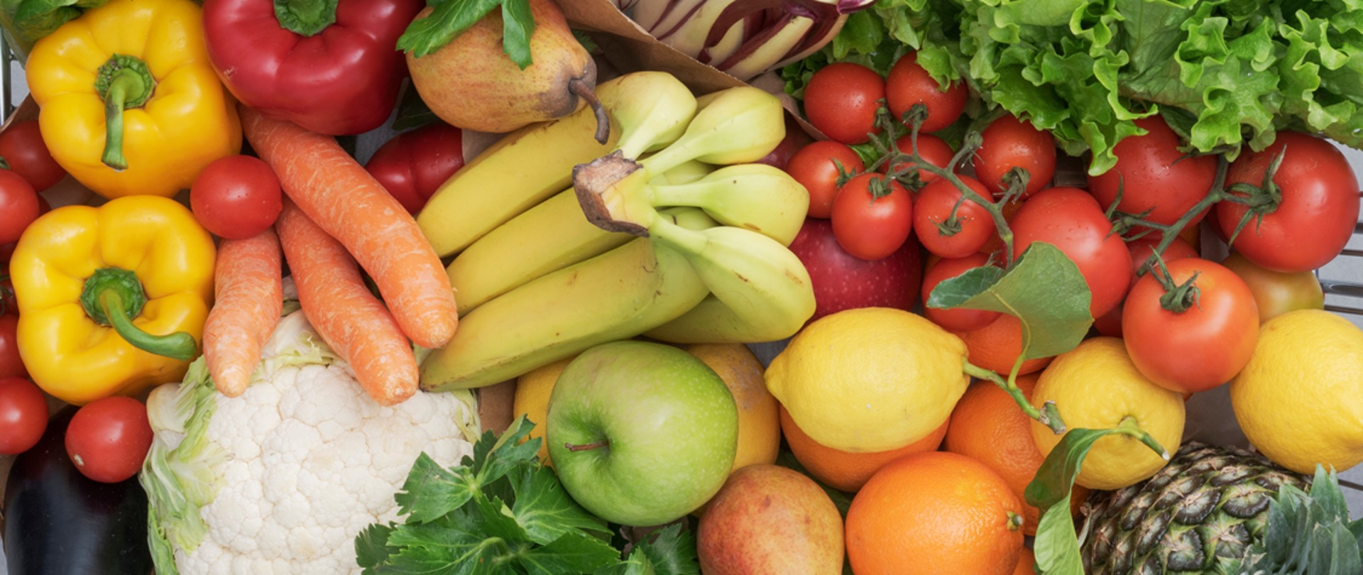 Na pierwszym planie rozpościera się obfitość świeżych owoców i warzyw, ułożonych w sposób tworzący apetyczną i harmonijną kompozycję. 