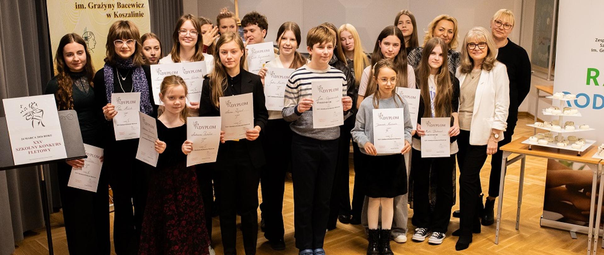 Uczniowie stoją z dyplomami, podłoga drewniana