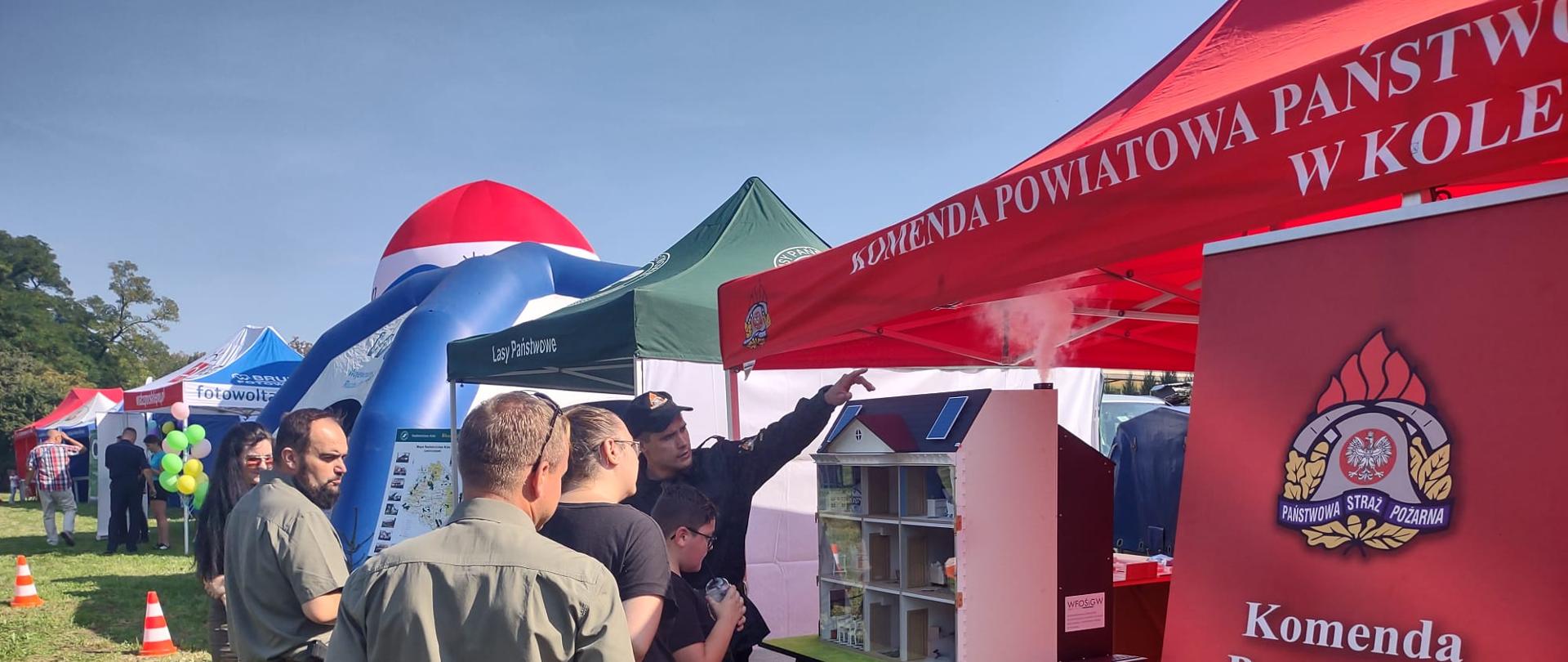 Zdjęcie przedstawia strażaka z Komendy Powiatowej Państwowej Straży Pożarnej w Kole udzielającego przybyłym na piknik osobom pokazu symulatora zagrożeń pożarowych