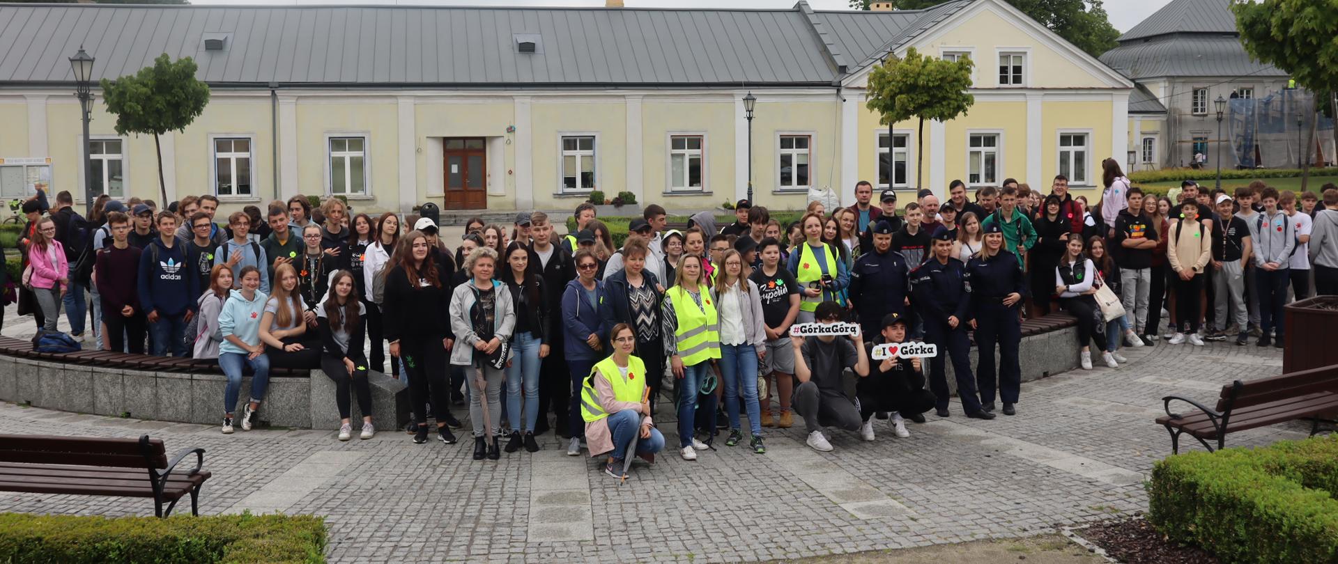 Na tle niskich budynków Urzędu Miasta w Końskich grupa ponad 100 osób, uczniów szkół ponadpodstawowych i ich opiekunów, przed wyruszeniem na rajd profilaktyczny.